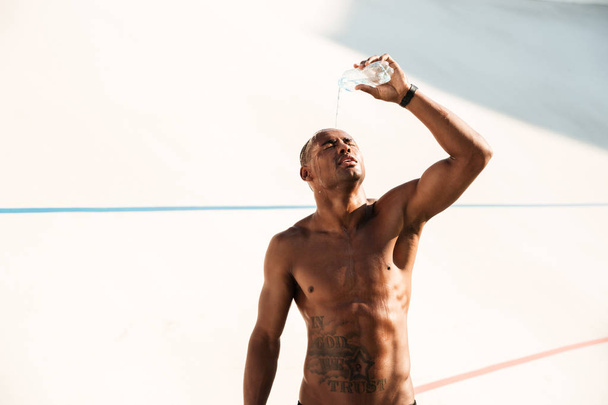 Photo of young african sports man pouring out water on his head - Foto, imagen