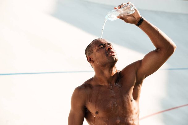 Close-up photo of young african sports man pouring out water on  - Foto, imagen