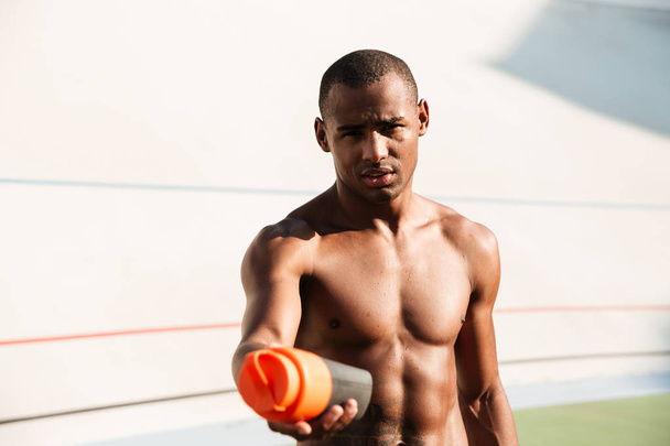 Close-up photo of half naked african sports man holdin bottle of - Zdjęcie, obraz