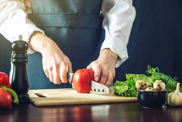 The chef in black apron cuts vegetables. Concept of eco-friendly products for cooking - Zdjęcie, obraz