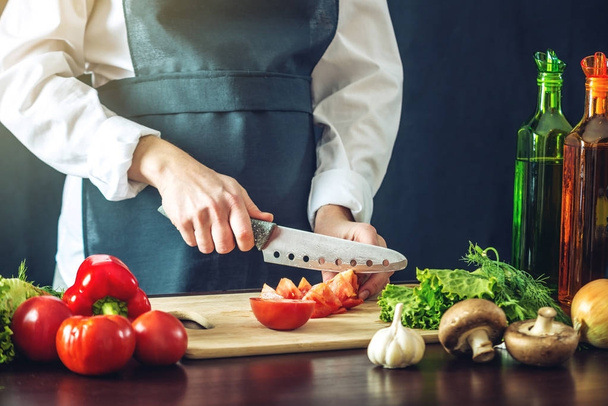 The chef in black apron cuts vegetables. Concept of eco-friendly products for cooking - Photo, Image