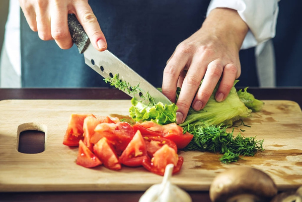 ブラック エプロンのシェフは野菜をカットします。調理のための環境に優しい製品のコンセプト - 写真・画像