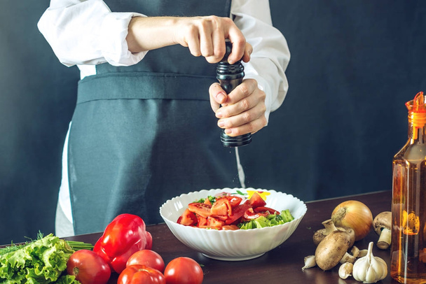 O chef de avental preto faz uma salada de legumes. Conceito de produtos ecológicos para cozinhar
 - Foto, Imagem