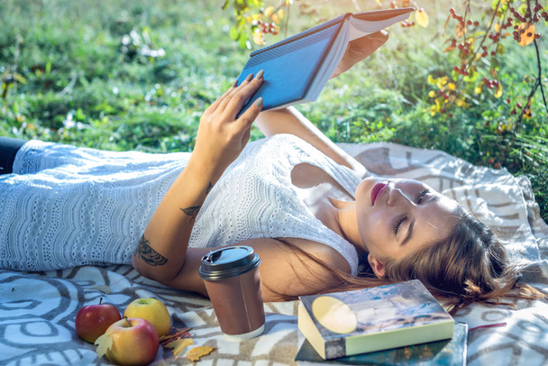 Frau liest ein interessantes Buch, das an einem sonnigen Sommertag im Park auf einem grünen Rasen liegt. Konzept der studentischen Ausbildung - Foto, Bild