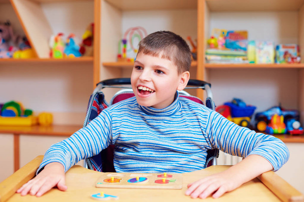 cheerful boy with disability at rehabilitation center for kids with special needs, solving logical puzzle - Foto, immagini