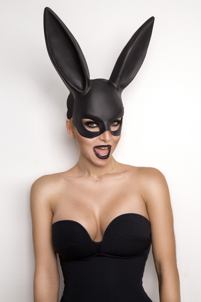 sexy Frau mit großen Brüsten trägt eine schwarze Maske Osterhase steht auf weißem Hintergrund und sieht sehr sinnlich - Foto, Bild