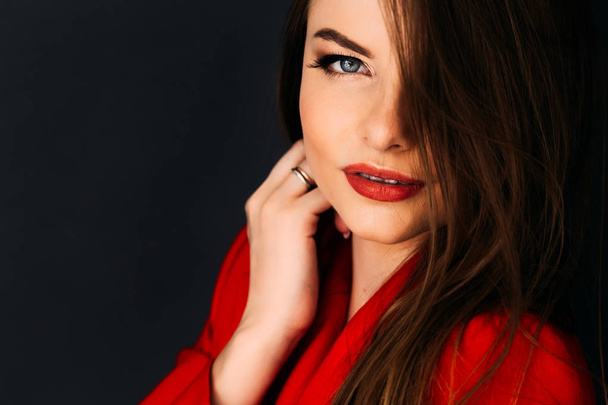 Krásný model v červené bundě s červenými rty na tmavém pozadí  - Fotografie, Obrázek
