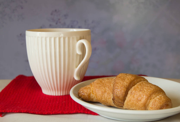 Desayuno de Navidad - Copa blanca y croissant sobre un fondo de bufanda de punto rojo
 - Foto, Imagen