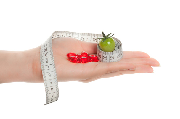 Woman's hands holding green tomato, pills with measuring tape - Photo, Image