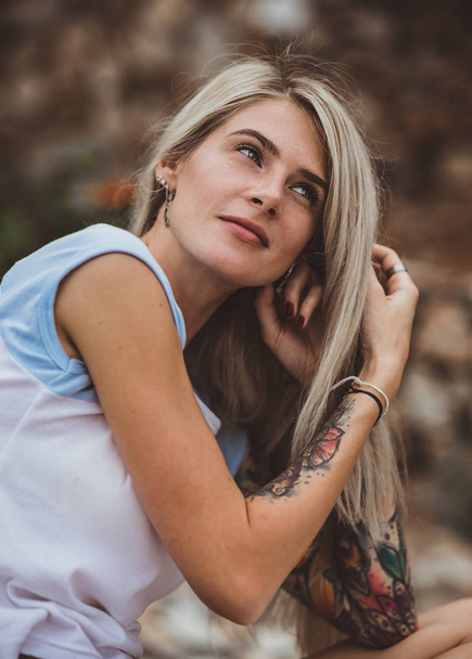 Beautiful blonde woman sitting on a stone embankment and reads book. Hands tattooed. modern, trendy, student. Closeup portrait - Fotoğraf, Görsel