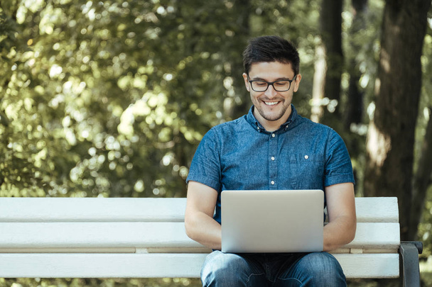 mladý muž s notebookem sedí v parku - Fotografie, Obrázek