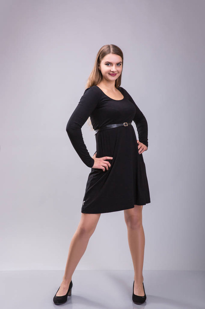 灰色の背景に黒のドレスでポーズをとってプラスのサイズの女性モデルのポートレート. - 写真・画像