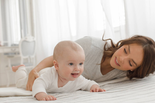 Mother and baby playing and smiling on bed - Photo, image