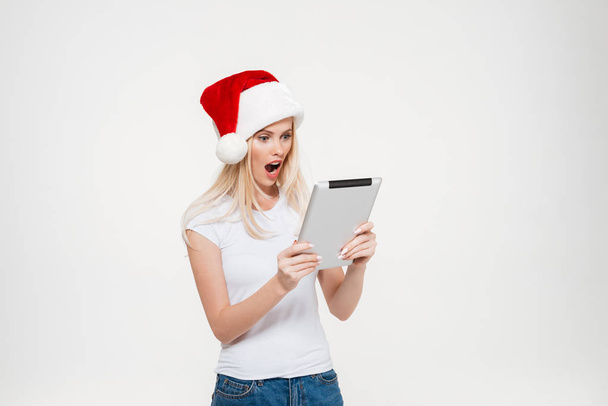 Portrait of a shocked excited woman in christmas hat using tablet - Фото, зображення