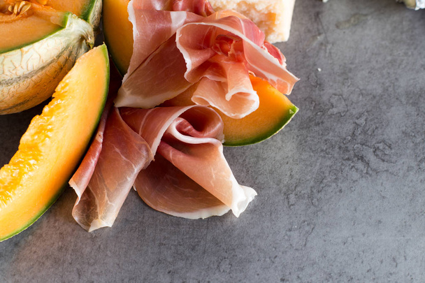 Jambon mix. Ham. Traditional Italian and Spanish salting, smoking, dry-cured dish - jamon Serrano and prosciutto crudo sliced with melon on grey background. Copy space. Closeup - Foto, imagen