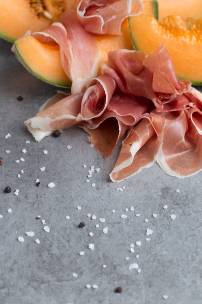 Jambon mix. Ham. Traditional Italian and Spanish salting, smoking, dry-cured dish - jamon Serrano and prosciutto crudo sliced with melon on grey background. Copy space. Closeup - Photo, Image