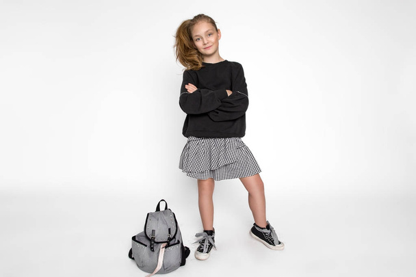 Roztomilá holčička v školní oblečení a školní batoh sedí na bílém pozadí - Fotografie, Obrázek