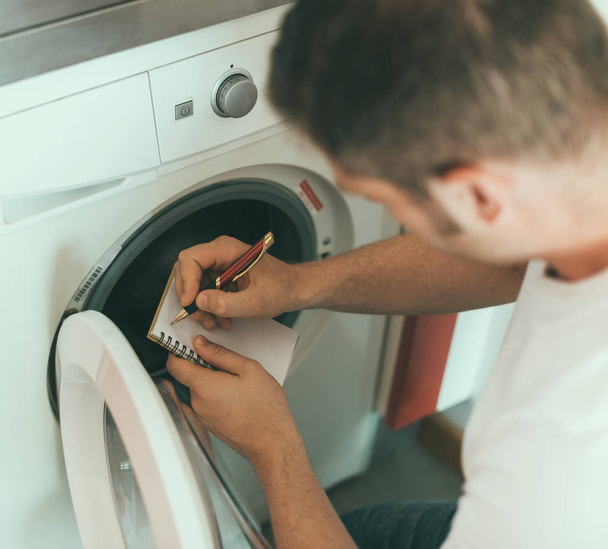 Técnico masculino reparando máquina de lavar roupa, escrevendo o código do fabricante
. - Foto, Imagem