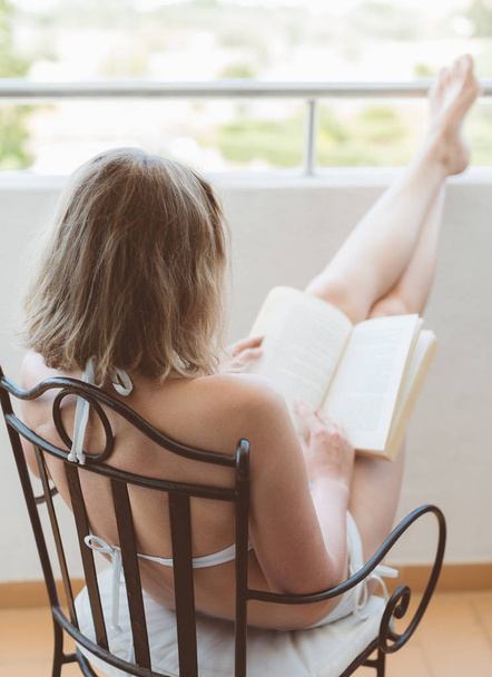 Γυναίκα διαβάζει το βιβλίο στο μπαλκόνι το καλοκαίρι. - Φωτογραφία, εικόνα