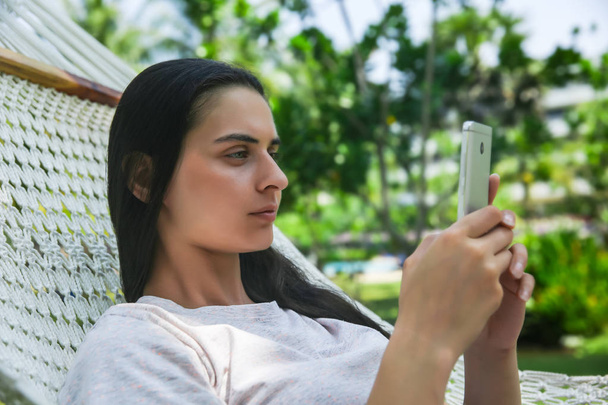 Relaxed young woman looking at mobile phone in hammock - Photo, Image
