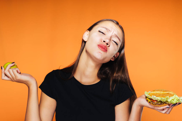 hungry girl sits on a diet, but eats an unhealthy high-calorie hamburger - Zdjęcie, obraz