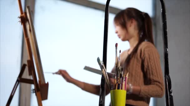 Nastolatek farby malowanie farbami na płótnie, który stoi na sztalugach - Materiał filmowy, wideo