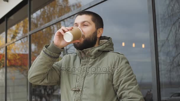 Un guapo joven barbudo sostiene una taza. beber café o té caliente en otoño al aire libre
 - Metraje, vídeo