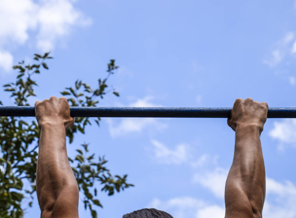 Hands on the bar close-up. The man pulls himself up on the bar. Playing sports in the fresh air. Horizontal bar - 写真・画像