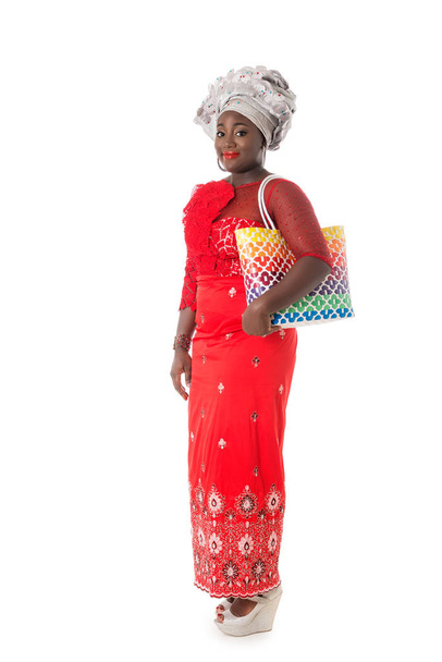 Beautiful African woman walking in traditional red clothing with tote bag,isolated - Fotó, kép