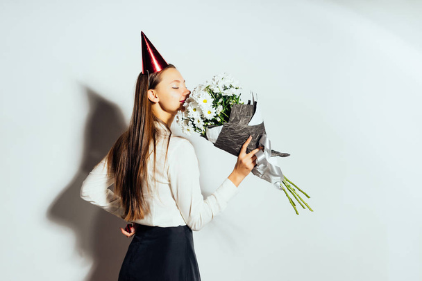 a nice girl with long hair received a beautiful bouquet of chamomiles as a birthday gift. a girl with a festive cap - Photo, image