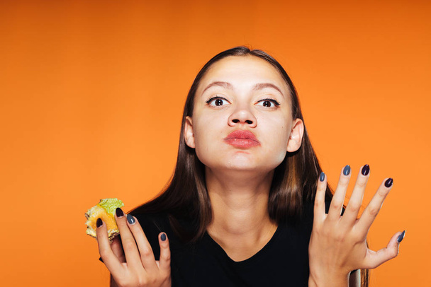 the hungry girl eats her hamburger.Very tasty food, isolated on an orange background - Foto, imagen