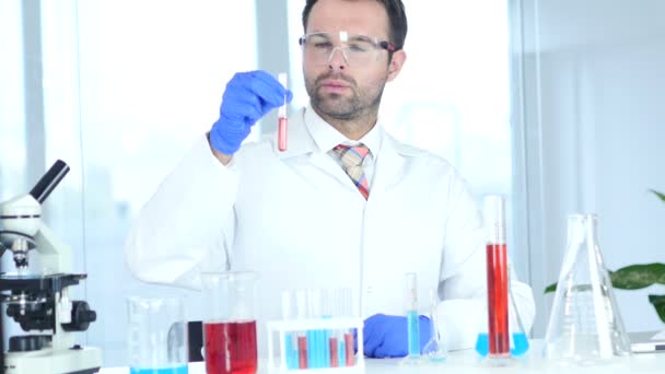 Vědec, lékař při pohledu na červené řešení ve zkumavce v laboratoři - Záběry, video