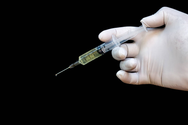 strzykawka w rękę w Rękawice medyczne, gotowy do wtrysku z lek. czarne tło - Zdjęcie, obraz
