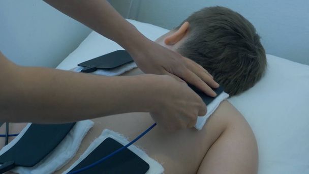 Electro stimulation in physical therapy. Physical therapist positioning electrodes for lower back muscle treatment. TENS electrodes treatment on back. - Photo, Image