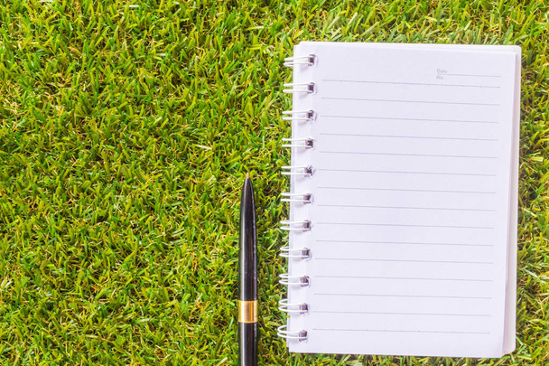 Pen on note book on grass background. - Photo, image