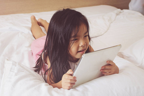 Azjatycki dziewczynka przy użyciu komputera typu tablet w łóżku - Zdjęcie, obraz