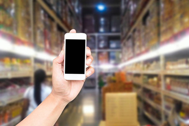 Male hand holding mobile smart phone on Supermarket blur background, business concept - Photo, Image