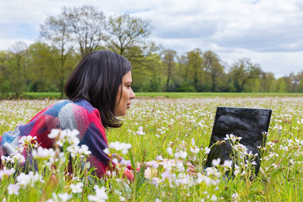 Frau mit Laptop liegt im Gras mit Blumen - Foto, Bild