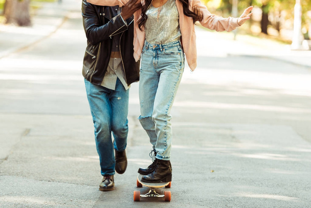 Vriendje helpen vriendin schaatsen op longboard   - Foto, afbeelding