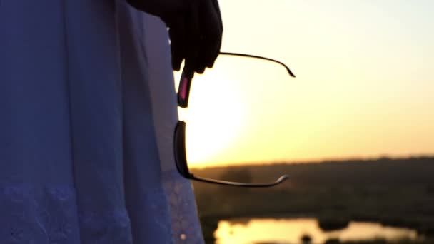 een jonge Brunette vrouw Stands met haar zonnebril en kijkt naar de zonsondergang in Slo-Mo - Video