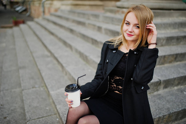 Elegant blonde girl wear on black posing at streets of town, sit - 写真・画像