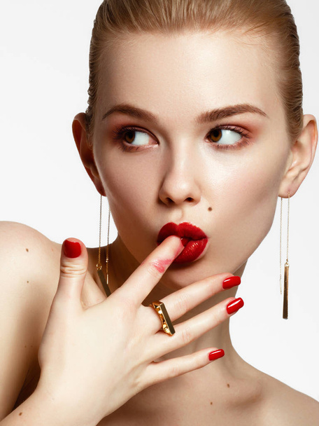 Makeup products. Young beautiful girl with gold earrings and ring smiling on white background. Red nails with manicure and white smile. Young woman with fashion accessories - Zdjęcie, obraz