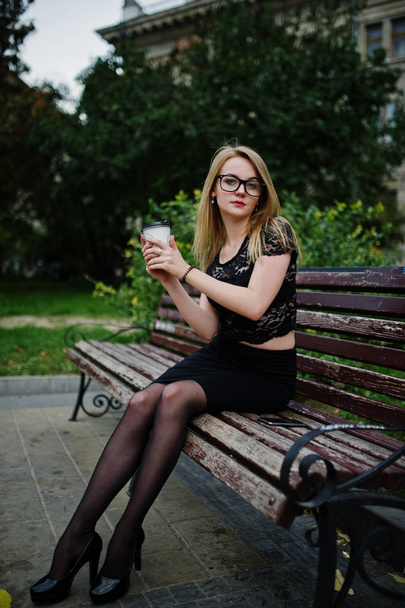 Elegant blonde girl wear on black posing at streets of town, sit - Photo, image