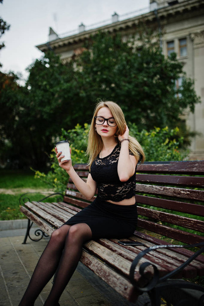 Elegant blonde girl wear on black posing at streets of town, sit - Foto, imagen