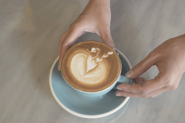 zbliżenie dłoni trzymając filiżanki kawy latte art na stole. - Zdjęcie, obraz