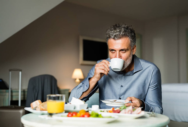 Mature businessman having breakfast in a hotel room. - Фото, зображення