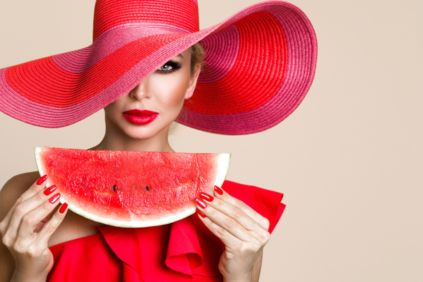 Prachtige vrouwelijke model met perfecte gezicht en rode hoed houden van een watermeloen op haar gezicht - Foto, afbeelding