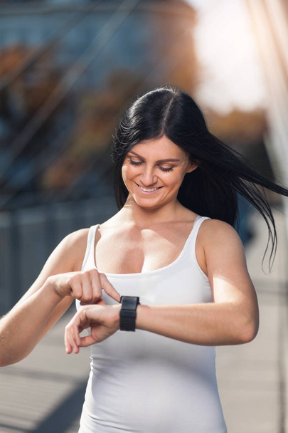 City workout. Beautiful woman with a smartwatch training in an urban setting - Foto, Imagen