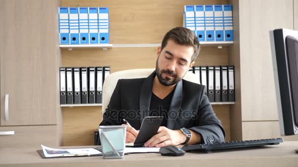 Молодой бизнесмен в своем офисе делает заметки в бумажном блокноте
 - Кадры, видео