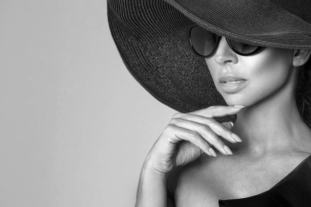 Portréja egy elegáns nő egy kalapot és napszemüveget, egy bézs háttérrel - Fotó, kép